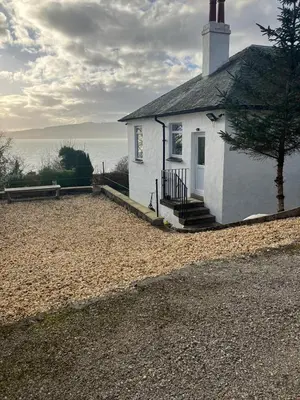 a small white house with a staircase next to the water at Dunholm Cottage in Skelmorlie