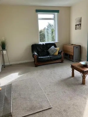 a living room with a black leather couch and a window at Dunholm Cottage in Skelmorlie