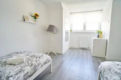 a white bedroom with two beds and a window at Woodside Apartment in Coatbridge