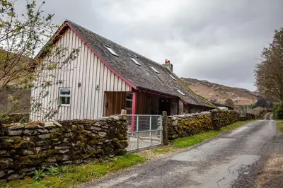 a barn with a stone wall next to a road at Kennels Cottage in Killin