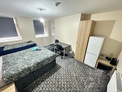 a bedroom with a bed and a desk and a refrigerator at Rangers GuestHouse in Glasgow