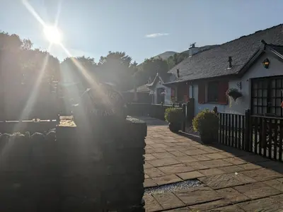 a sun shining on a house with a brick driveway at Heather Cottage Luss in Luss