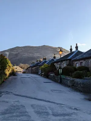 an empty street with houses and a mountain in the background at Heather Cottage Luss in Luss