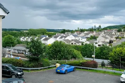 a blue car parked in a parking lot with houses at Super Prime Train Station Inverkeithing by TBA in Inverkeithing