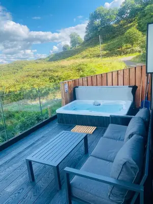 a hot tub on a deck with a bench and a table at The Black Cabin Oban in Oban