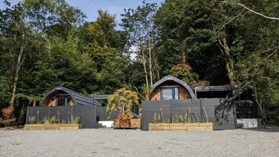 a house with a fence and trees in the background at Beach House Pods in Dunoon