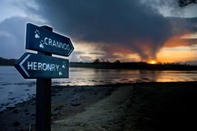 a couple of street signs on a beach with the sunset at Isle of Eriska Hotel Spa & Island in Benderloch