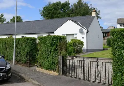 a white house with a fence and bushes at Ardview Cottage in Oban