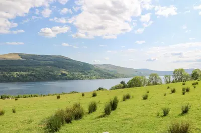 a grassy hill with a lake in the background at Beech Cottage in Aberfeldy