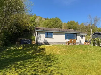 a small house on a grassy hill with a yard at Beech Cottage in Aberfeldy