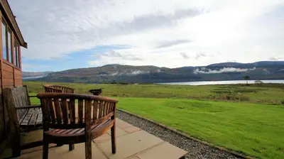 two benches sitting on a porch looking at a lake at Morenish Mews Killin Cottage in Morenish