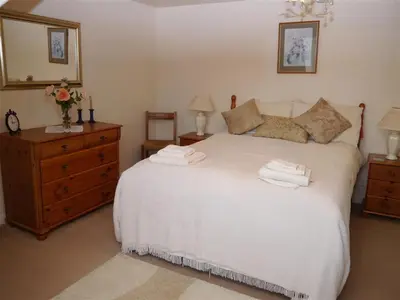 a bedroom with a white bed and a wooden dresser at Airie Farmhouse in Castle Douglas