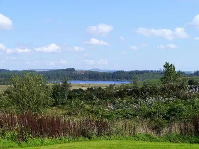 a view of a field with a lake in the distance at Airie Farmhouse in Castle Douglas