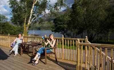 three women sitting at a table near a fence at Lochleven Seafood Cottage in Onich