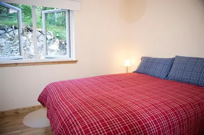 a bedroom with a bed with a red blanket and two windows at Lochleven Seafood Cottage in Onich