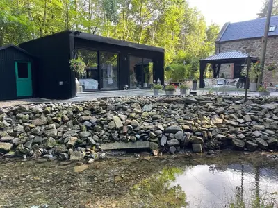 a black house with a stone wall next to a pond at The Ultimate Luss Retreat in Luss