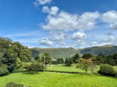 a green field with trees and mountains in the background at Woodlands House with Hot Tub in Ballachulish