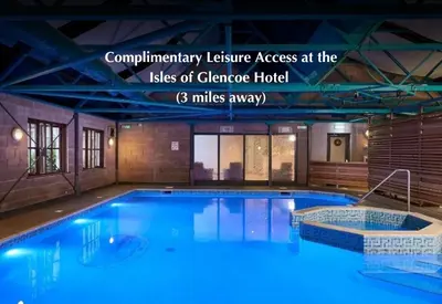 a large swimming pool with blue water in a building at Woodlands House with Hot Tub in Ballachulish