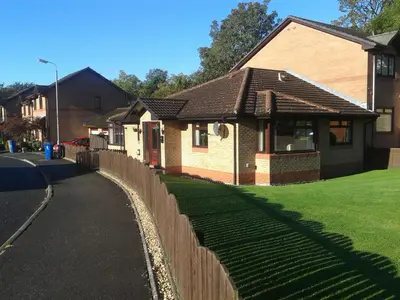 a brick house with a fence next to a yard at Dingieshowe Cottage in Lennoxtown
