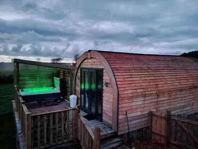 a large wooden building with a deck with a green light at The Galloway Steading - The Herons Nest, secure garden and with Hot Tub and Fire Pit in Glenluce