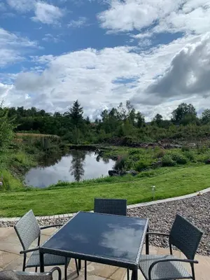 a table and chairs on a patio with a pond at Red Squirrel Pod with Hot Tub in Oban