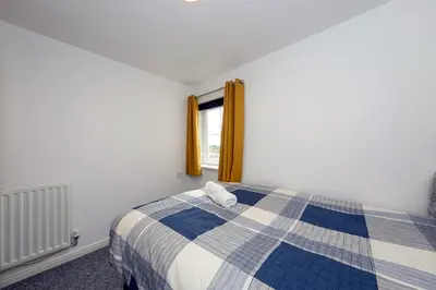 a bedroom with a blue and white bed with a window at Prime Duloch 2nd Floor Apartment by TBA in Fife