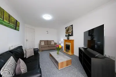 a living room with a black couch and a tv at Prime Duloch 2nd Floor Apartment by TBA in Fife