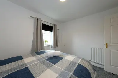a bedroom with a bed with a plaid blanket and a window at Prime Duloch 2nd Floor Apartment by TBA in Fife