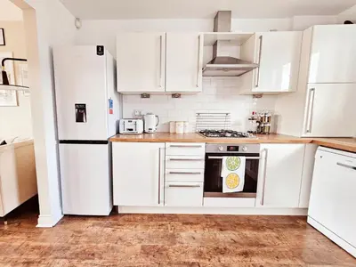 a white kitchen with white appliances and wooden floors at Modern 5 Bedroom Townhouse with Free Parking in Glasgow