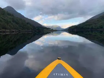 a paddle boat on a river with mountains in the background at West Highland Snug in Kinlochleven