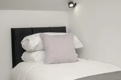 a white bed with a black headboard and white pillows at Historical Holmehill Lodge in Dunblane