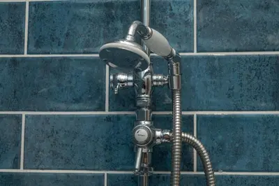a shower head in a bathroom with blue tiles at Historical Holmehill Lodge in Dunblane