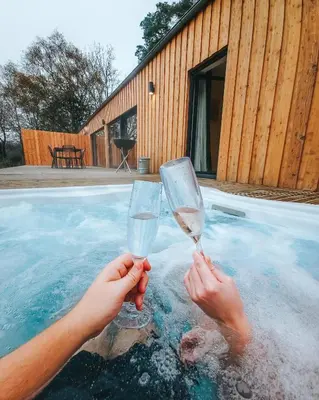 a person holding two wine glasses in a swimming pool at Forest Corner Luxury Home with Hot Tub in North Ballachulish