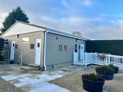a small gray building with a white fence at Red Deer Village Holiday Park - 2 Bedroom, Self-Catering Chalet in Steps
