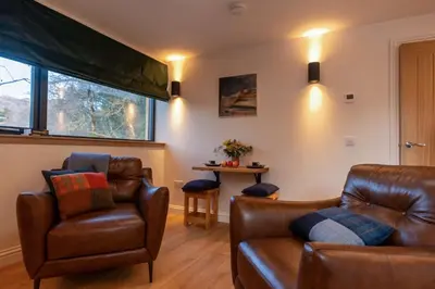 a living room with leather furniture and a table at Forest Corner Luxury Apartment with Hot Tub in North Ballachulish