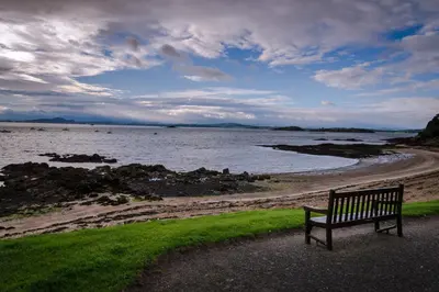 a bench sitting next to a body of water at Blacksands Seaview Cottage, Aberdour in Aberdour