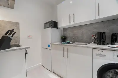 a kitchen with white cabinets and a washer and dryer at Dyke Apartment in Bailleston