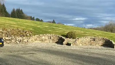 a stone bridge in a field with a grassy hill at Sheildaig Farm in Balloch