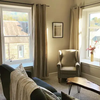 a living room with a couch and a chair and two windows at Stunning Apartment in Callander in Callander