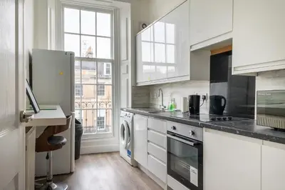 a kitchen with white cabinets and a washer and dryer at Bright High-Ceiling 2BD Flat - Central Edinburgh! in Edinburgh