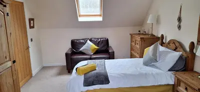 a bedroom with a bed and a leather chair at Ben Vorlich Cottage in Tarbet