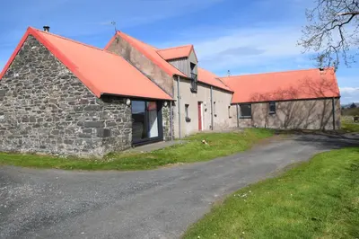 an old stone barn with a red roof and a road at The Byre at Drumachro in Isle of Gigha