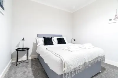 a white bedroom with a large white bed with black pillows at Bell Apartment in Airdrie