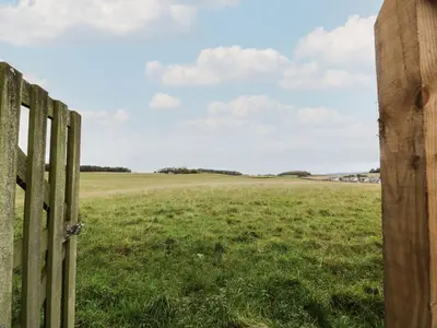 a wooden fence in a field with a field behind it at Thorneydyke Cottage in Stirling