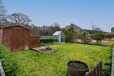 a garden with a wooden fence and a greenhouse at The Old Deanston Workers Cottage in Doune
