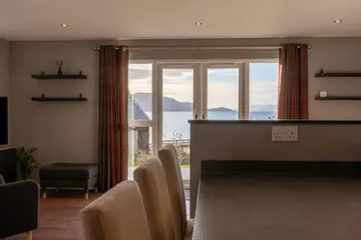 a living room with a table and chairs and a large window at Cairn Cottage in Onich