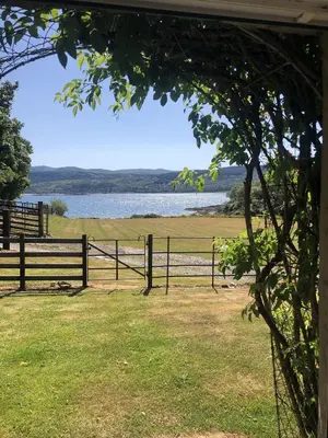 a fence with a view of a field and a lake at Ellary Cottage in Stonefield