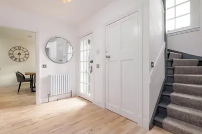 a white hallway with stairs and a round mirror at Stunning Dalchenna w/hot tub & huge garden in Stirling
