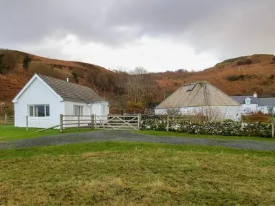 a white house and a barn with a fence at Ormsaig Byre in Beach