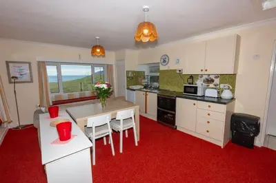 a kitchen with white cabinets and a red carpet at Ormsaig Byre in Beach